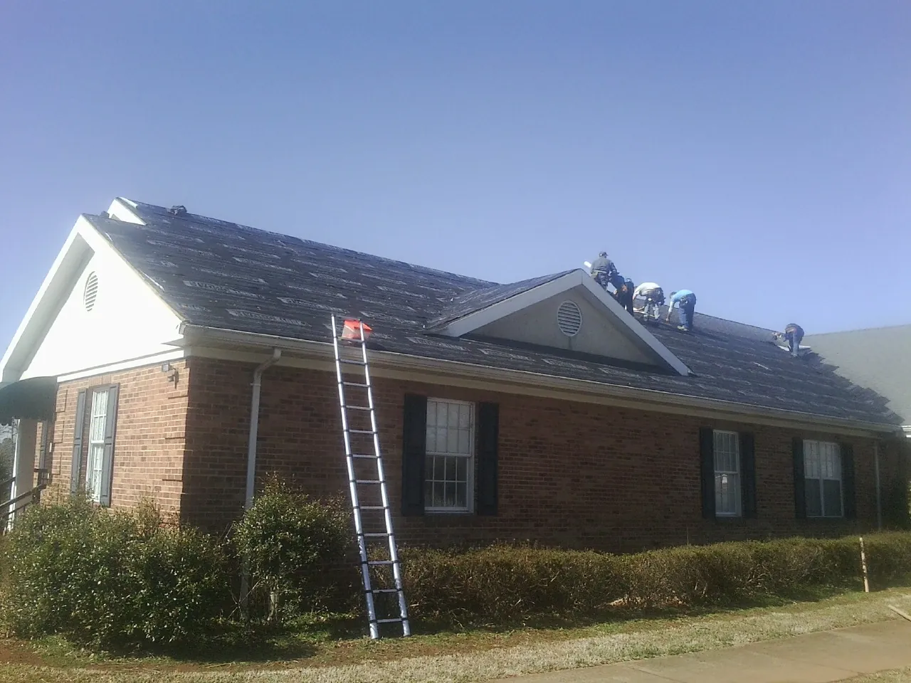 Crew tearing shingles off a brick ranch roof with a ladder set — Emergency Roof Repair work by our crew in Catawba