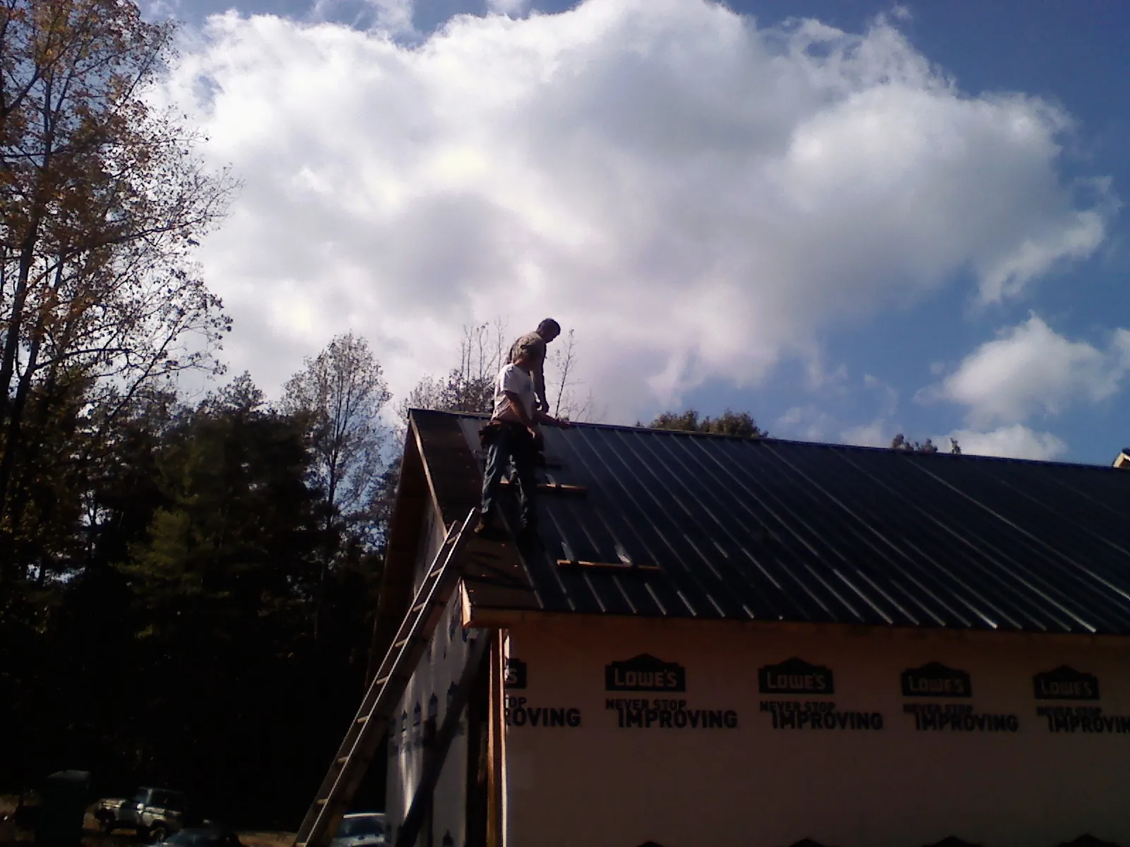Roofer fastening dark metal panels high against a cloudy sky, from a Roof Inspection job in Catawba
