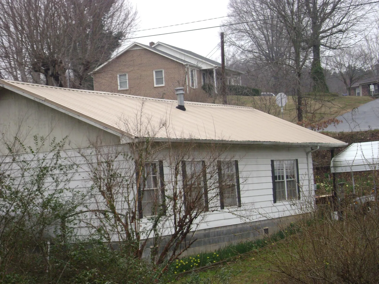 Tan metal roof on a white sided house set into a hillside — Commercial Roofing by Roofing Brothers in Catawba